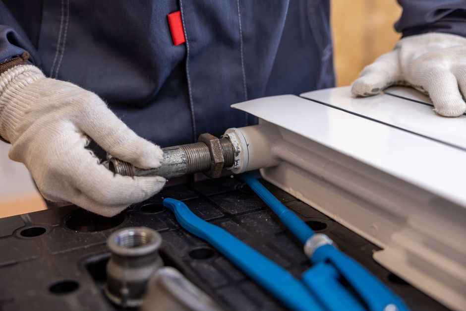 Technik v pracovním oděvu a rukavicích montuje šroubení vodovodní instalace